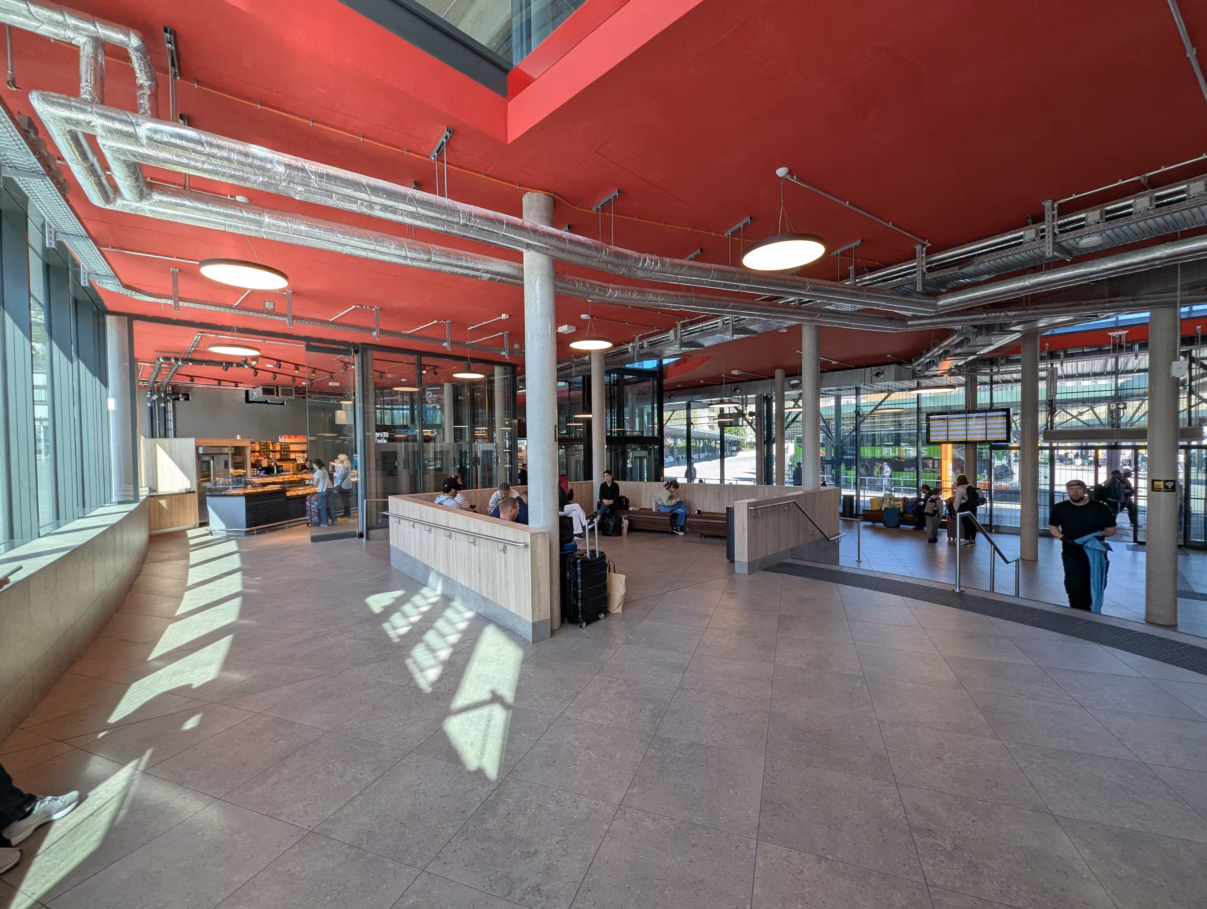 An interior shot of the waiting hall with a seating area, arrival board, and a glass front